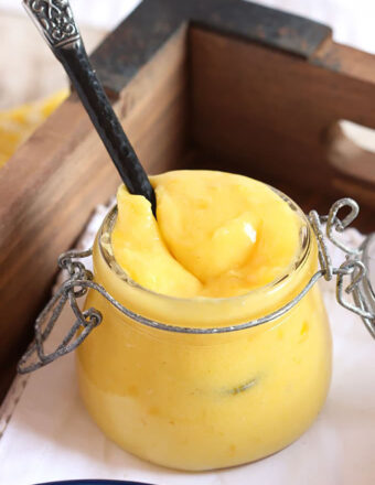 Lemon Curd in a jar with a spoon in it.