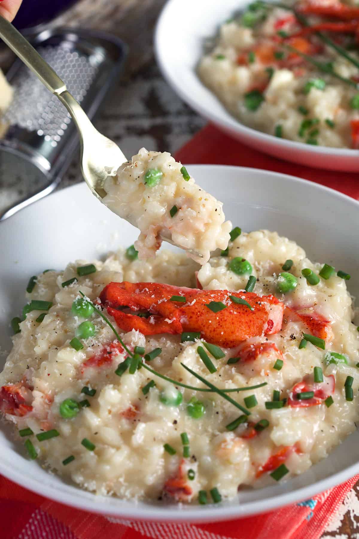 A fork is lifting a bite of lobster risotto from the bowl.