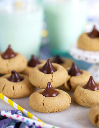 Peanut Butter Blossom cookies arranged on a white marble platter with polka dot straws and a glass of milk.