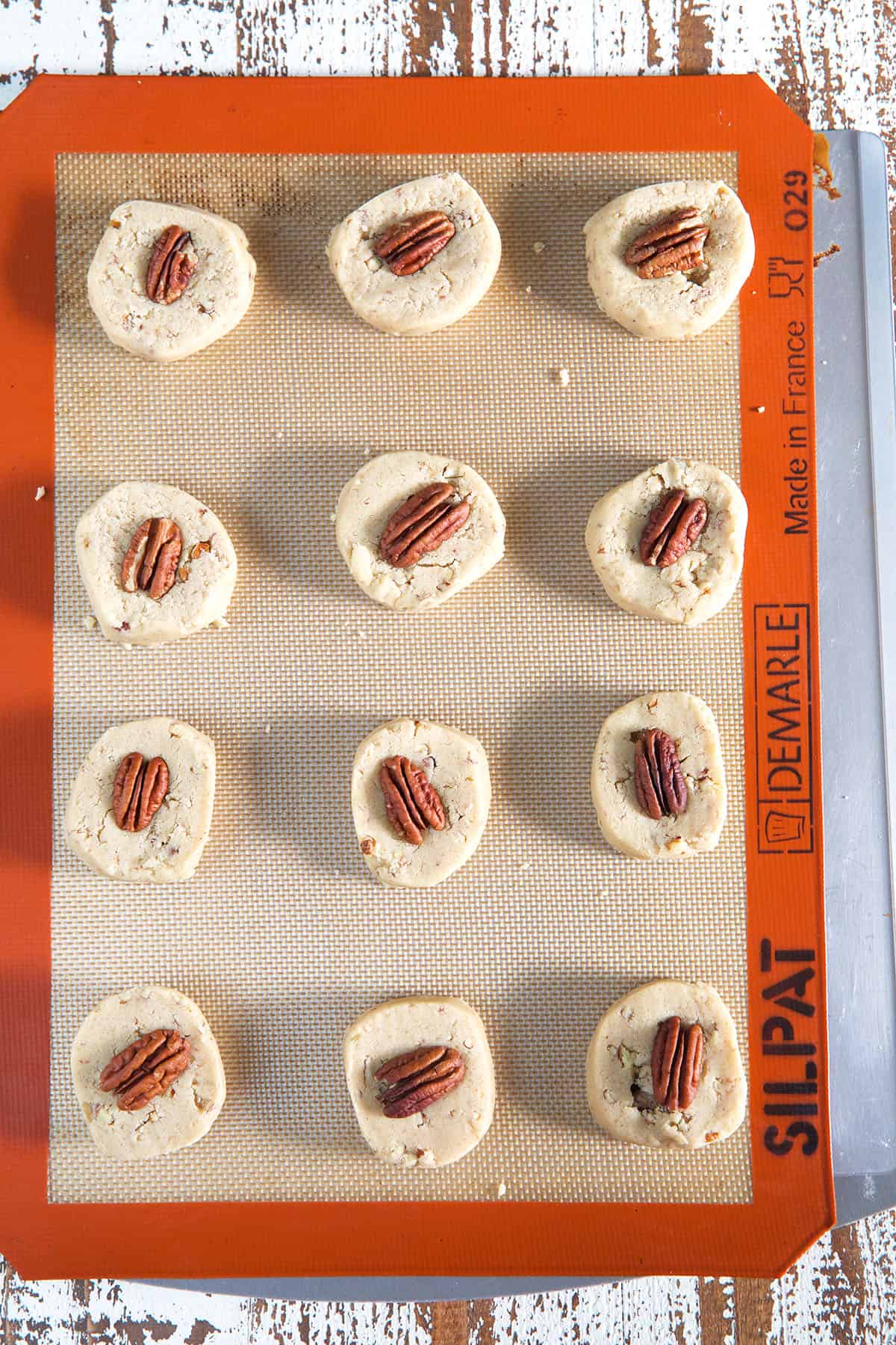 A dozen pecan sandies are placed on a siplat covered baking sheet.