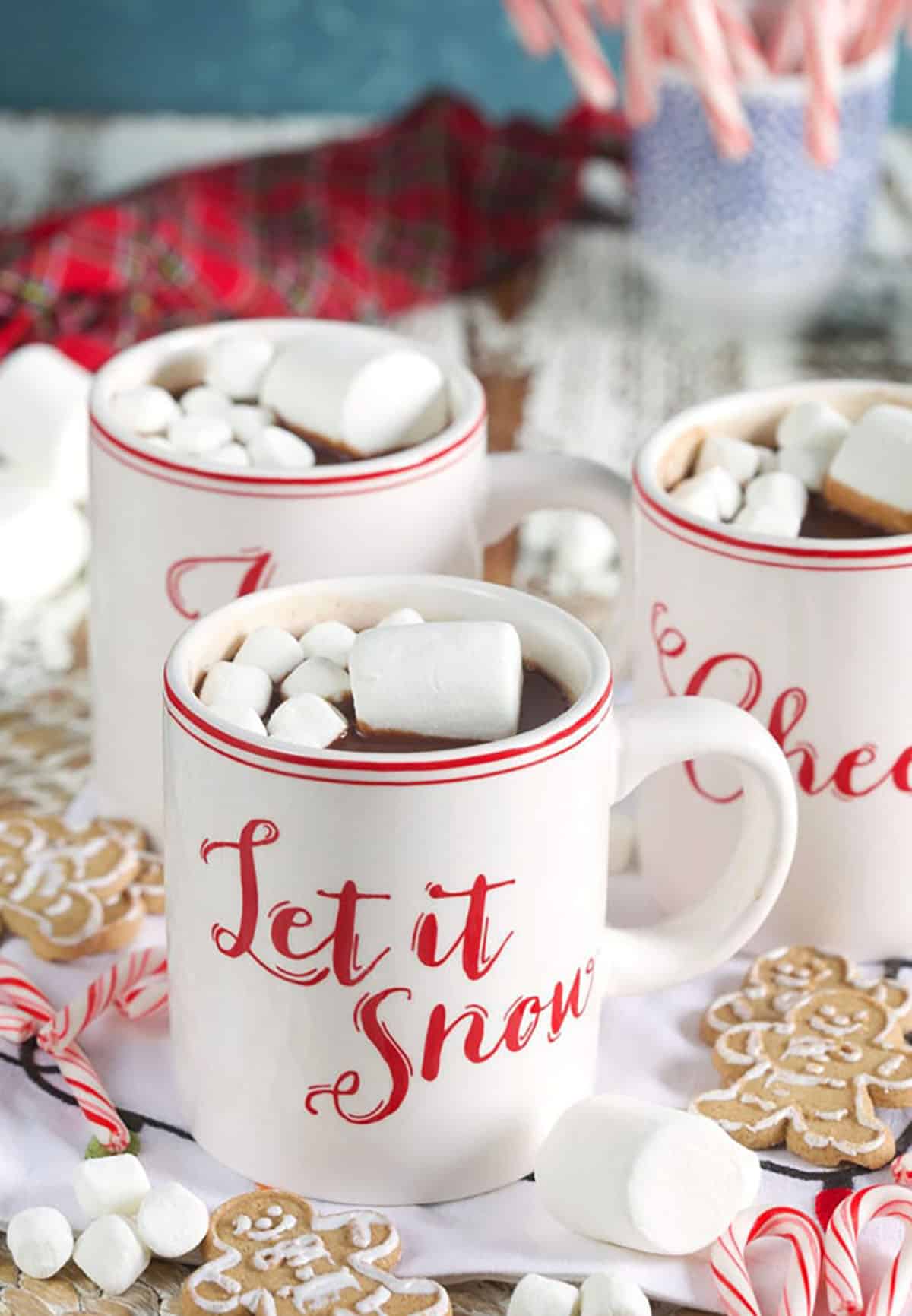 Three Christmas themed mugs are filled with hot chocolate and marshmallows. 
