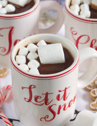 A mug that says "let is snow" in red lettering is filled with hot chocolate and marshmallows.