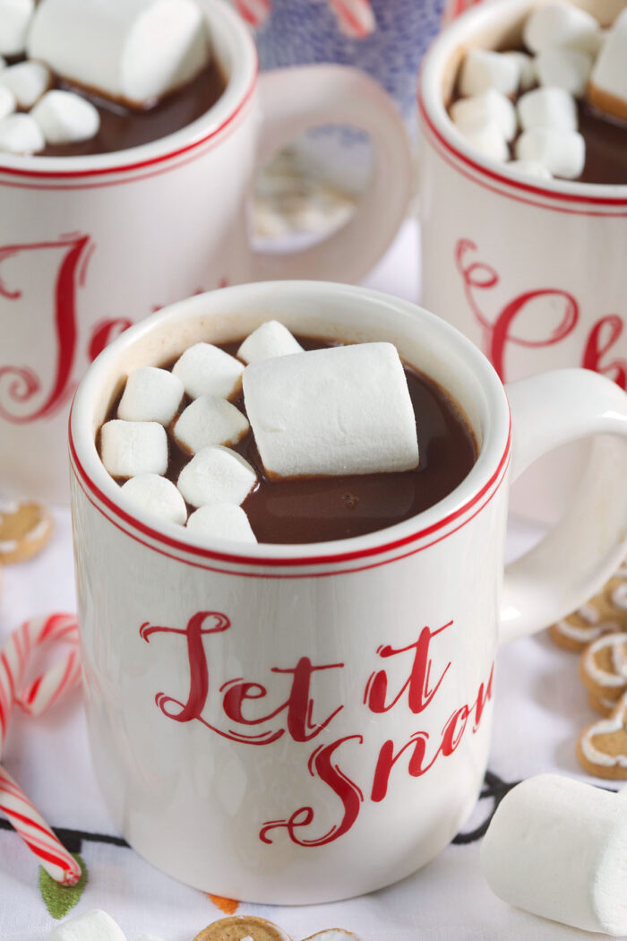 A mug that says "let is snow" in red lettering is filled with hot chocolate and marshmallows.