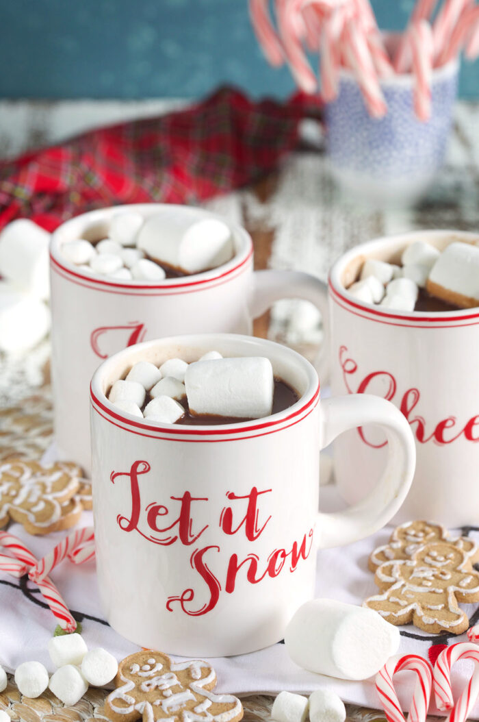 Three Christmas themed mugs are filled with hot chocolate and marshmallows. 