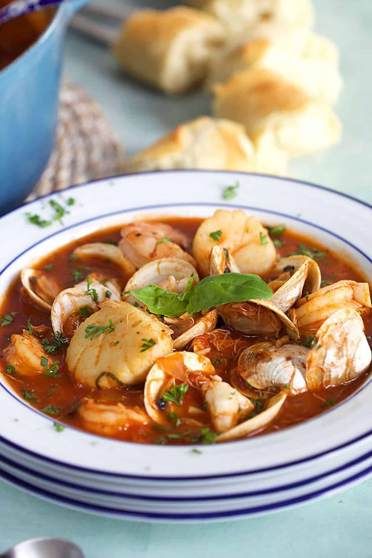 Stacked bowls with the top bowl filled with cioppino with crusty bread in the background.