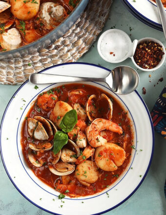 White bowl with Seafood Cioppino with a silver soup spoon on the side of the bowl.