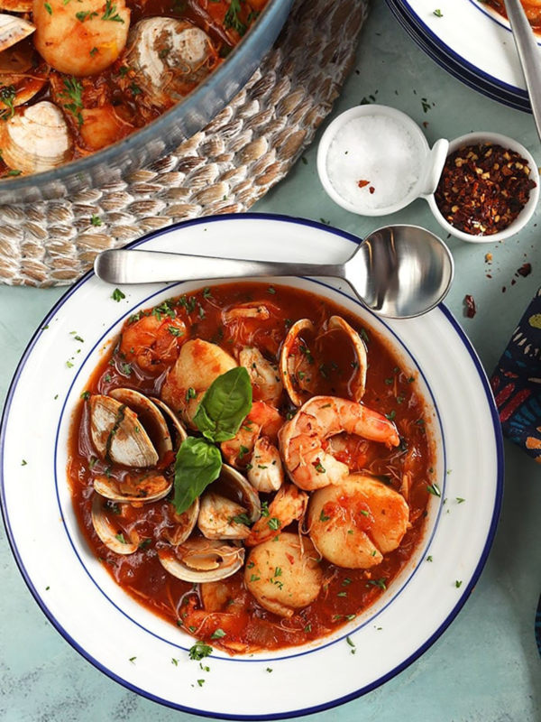 White bowl with Seafood Cioppino with a silver soup spoon on the side of the bowl.