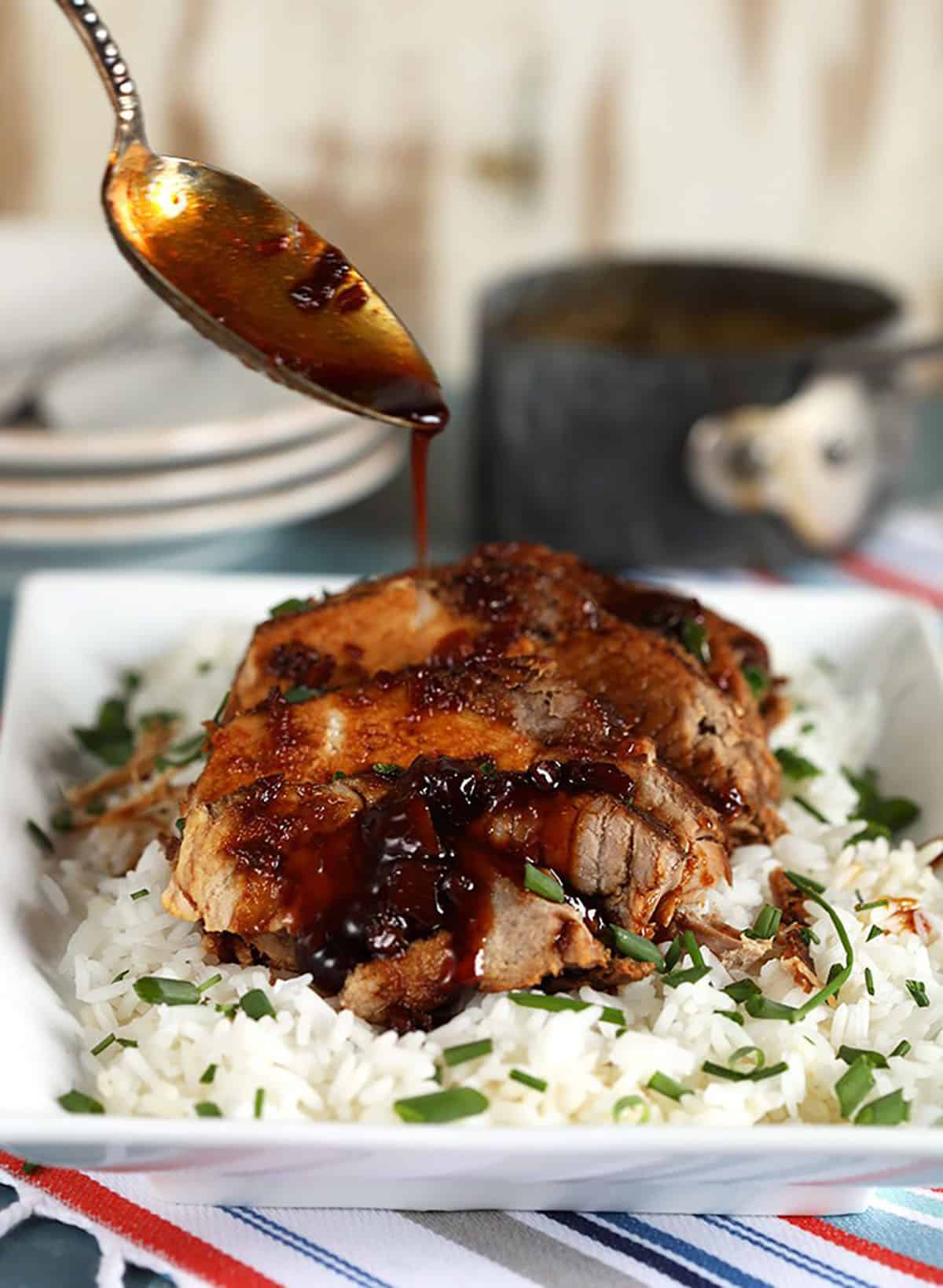 Honey garlic sauce being drizzled over Crock Pot Pork Loin Roast on a bed of white rice.