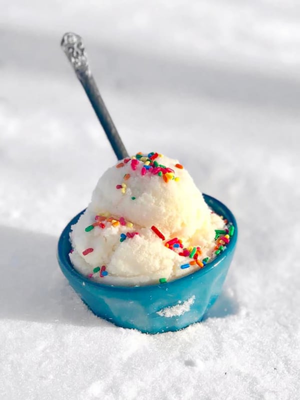 Snow ice cream in a blue bowl with a spoon and topped with sprinkles in the snow.