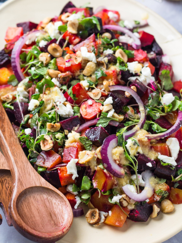 Beet salad is placed on an oval shaped serving platter with a set of wooden salad servers.