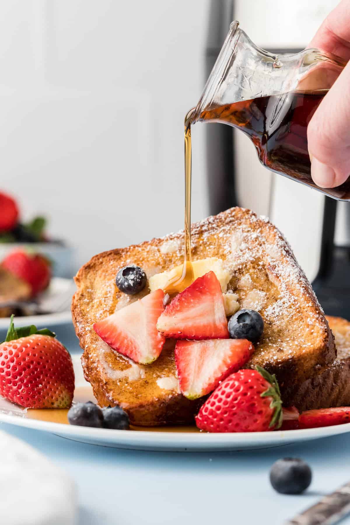 Syrup is being drizzled on top of a serving of french toast with berries.