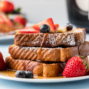 A stack of french toast is topped with syrup and berries on a white plate.