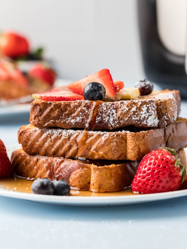A stack of french toast is topped with syrup and berries on a white plate.