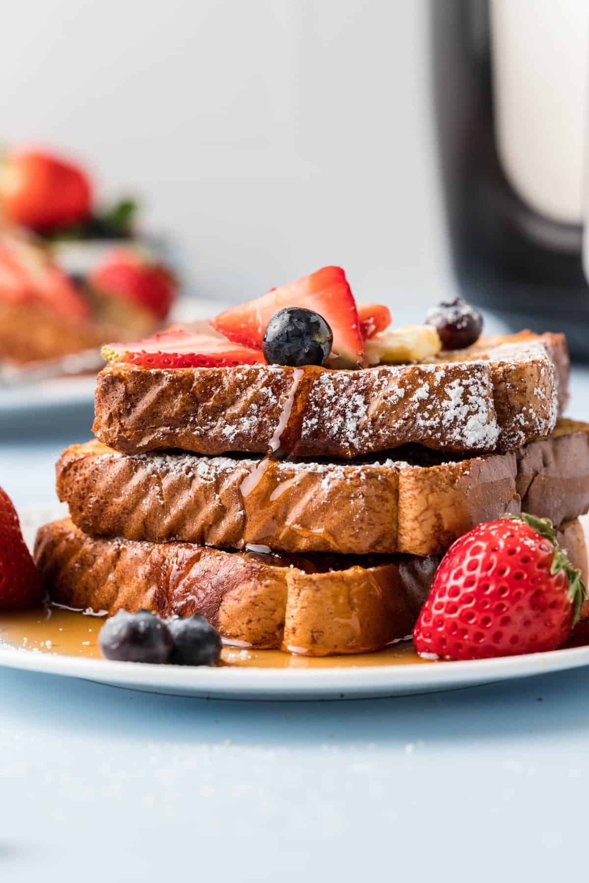 A stack of french toast is topped with syrup and berries on a white plate.
