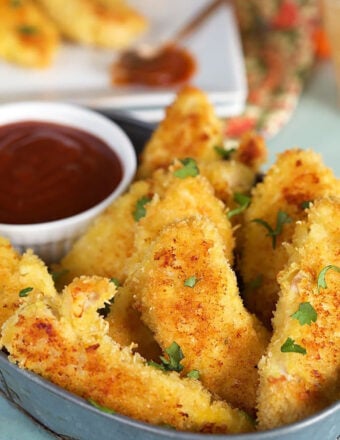 Close up of crispy chicken tenders in a metal tray with a bowl of barbecue sauce in it.