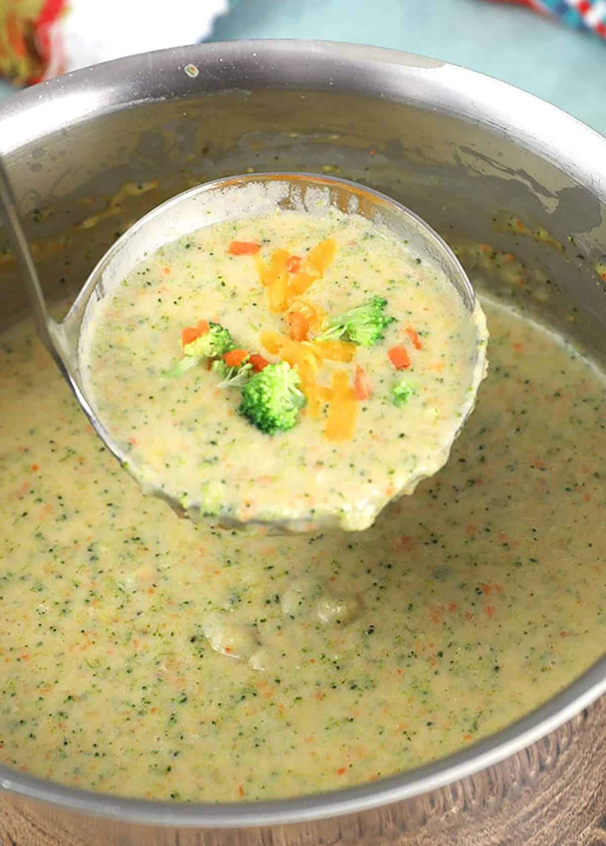 Big pot of broccoli cheddar soup with a ladle scooping a serving.
