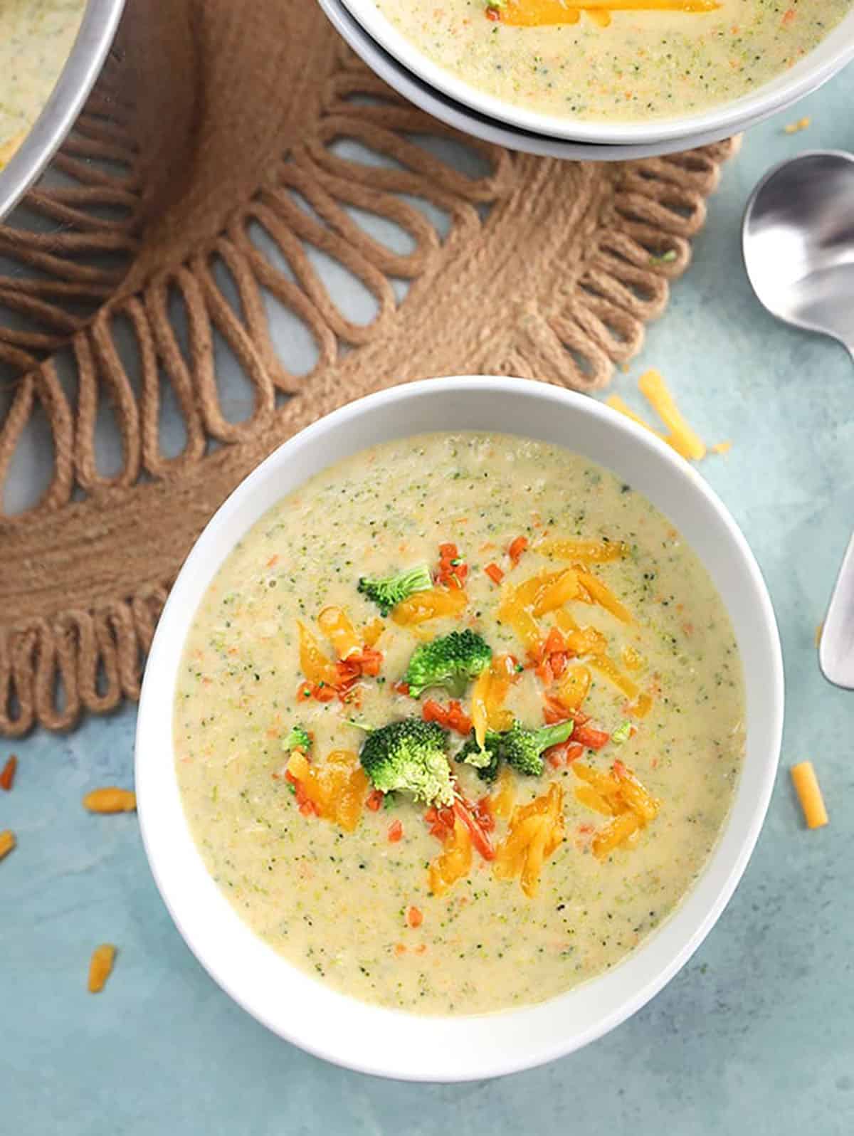 Broccoli Cheddar soup in a white bowl with a spoon on a blue background.