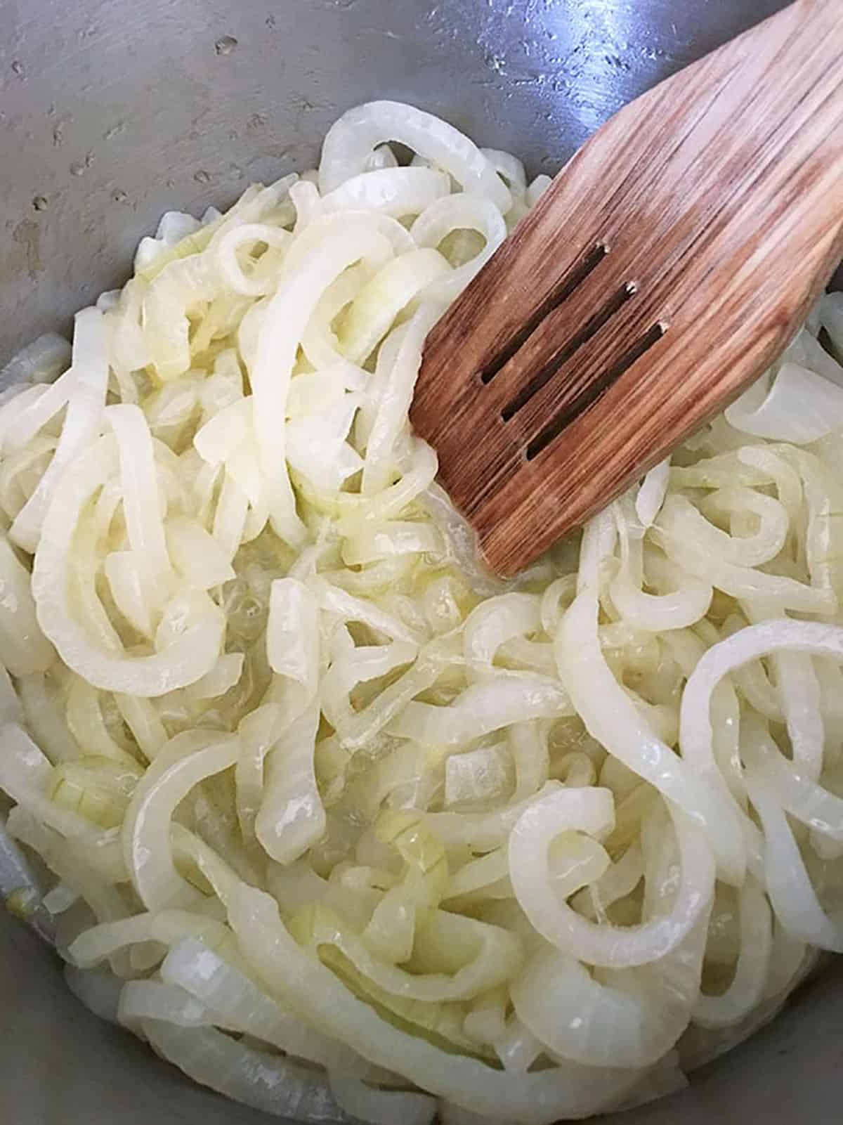 cooked sliced onions in a pot with a wooden spoon.