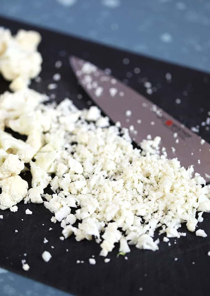 Cauliflower Rice on a black cutting mat with a knife