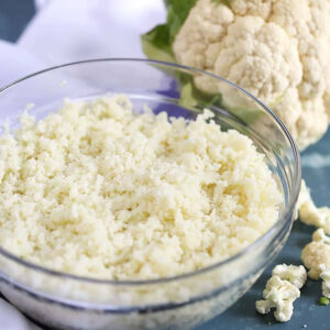 Glass bowl of cauliflower rice on a blue background