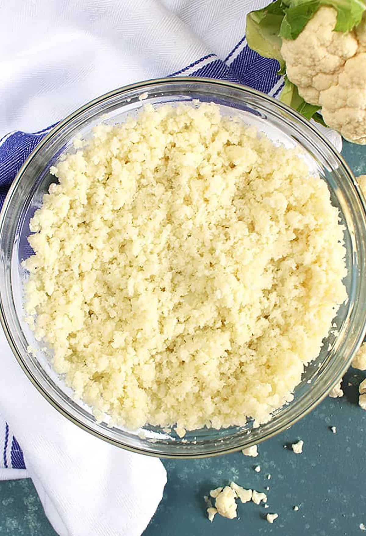 Overhead shot of cauliflower rice in a glass bowl on a blue background