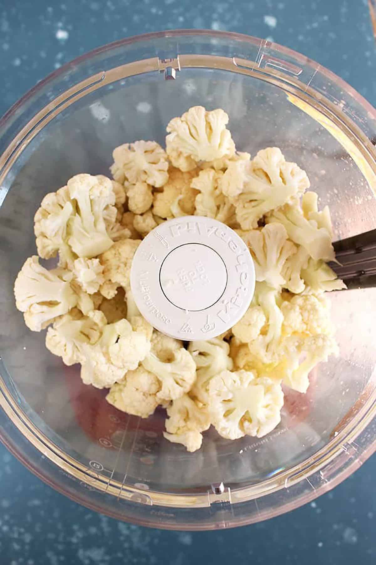 Overhead shot of cauliflower florets in a food processor bowl 