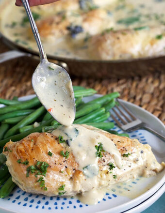 Chicken florentine on a plate with green beans and a spoon pouring sauce over the chicken.