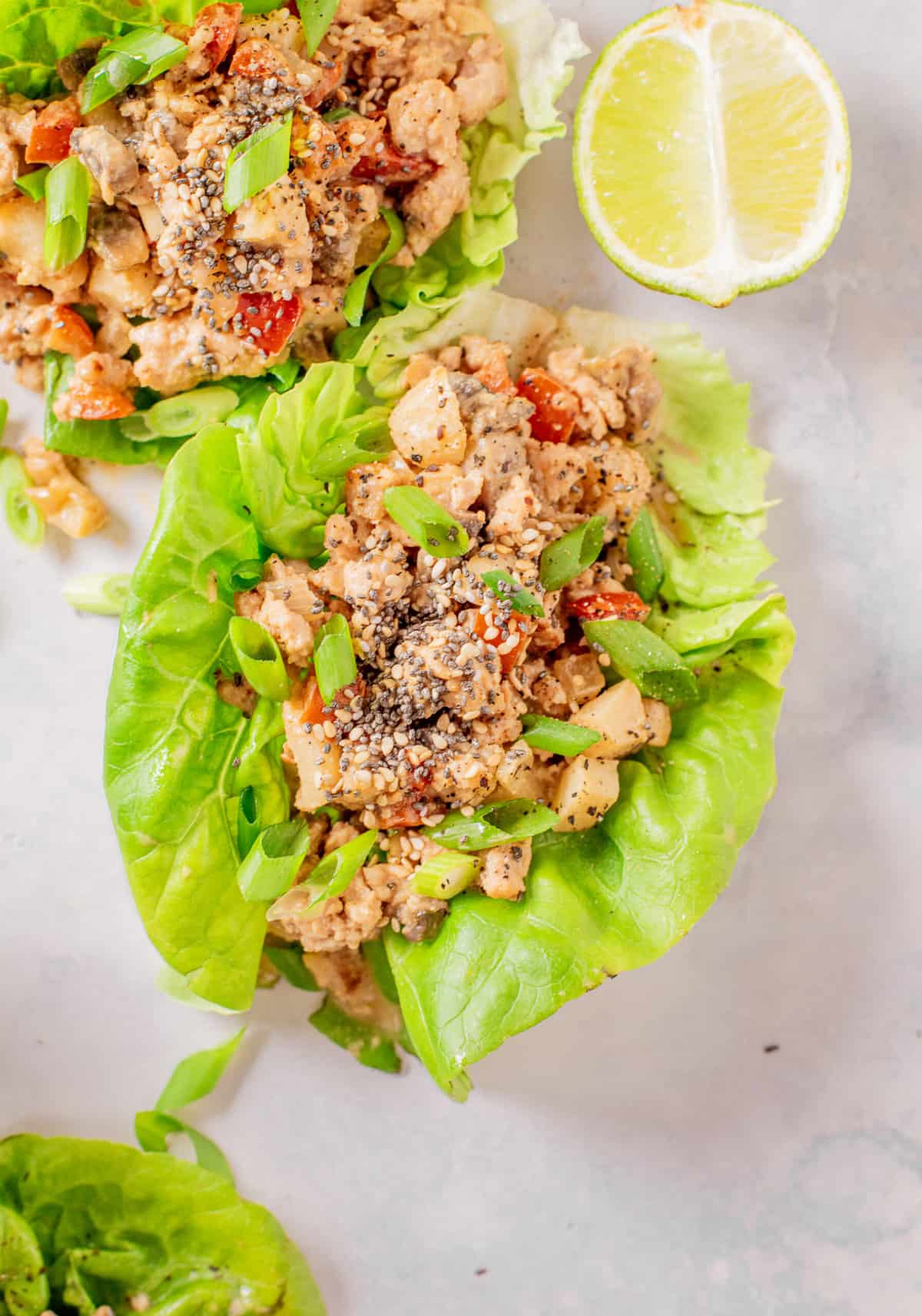 Two chicken lettuce wraps are placed next to a slice of lime.