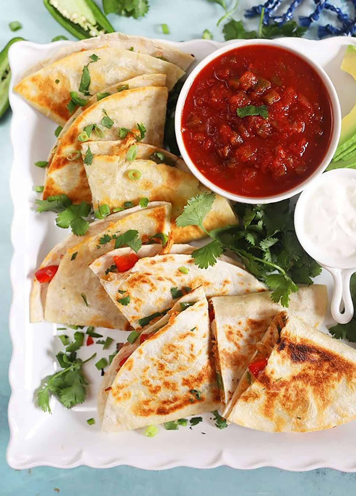 Overhead shot of chicken quesadillas on a square white platter with salsa.