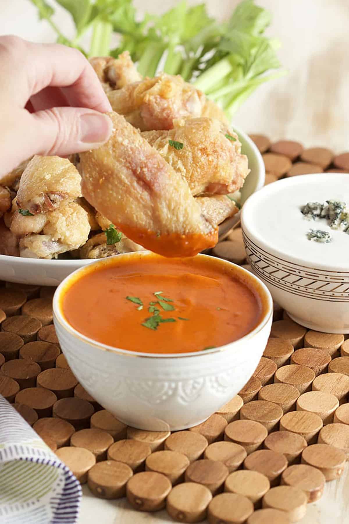 Crispy Baked Chicken Wing being dipped into a bowl of buffalo sauce.