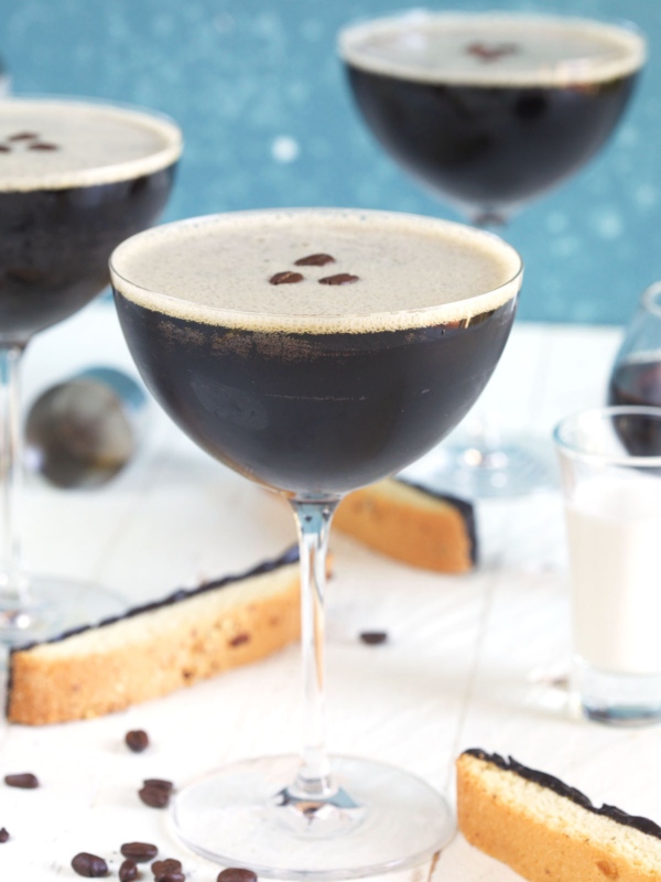 Several full martini glasses are placed next to biscotti on a white countertop.