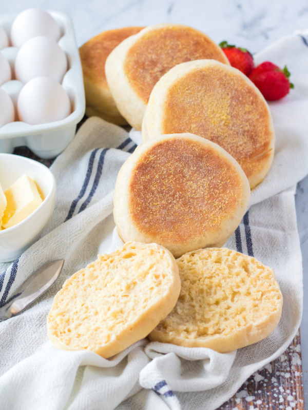 Several whole muffins are placed to a halved muffin on a white surface.
