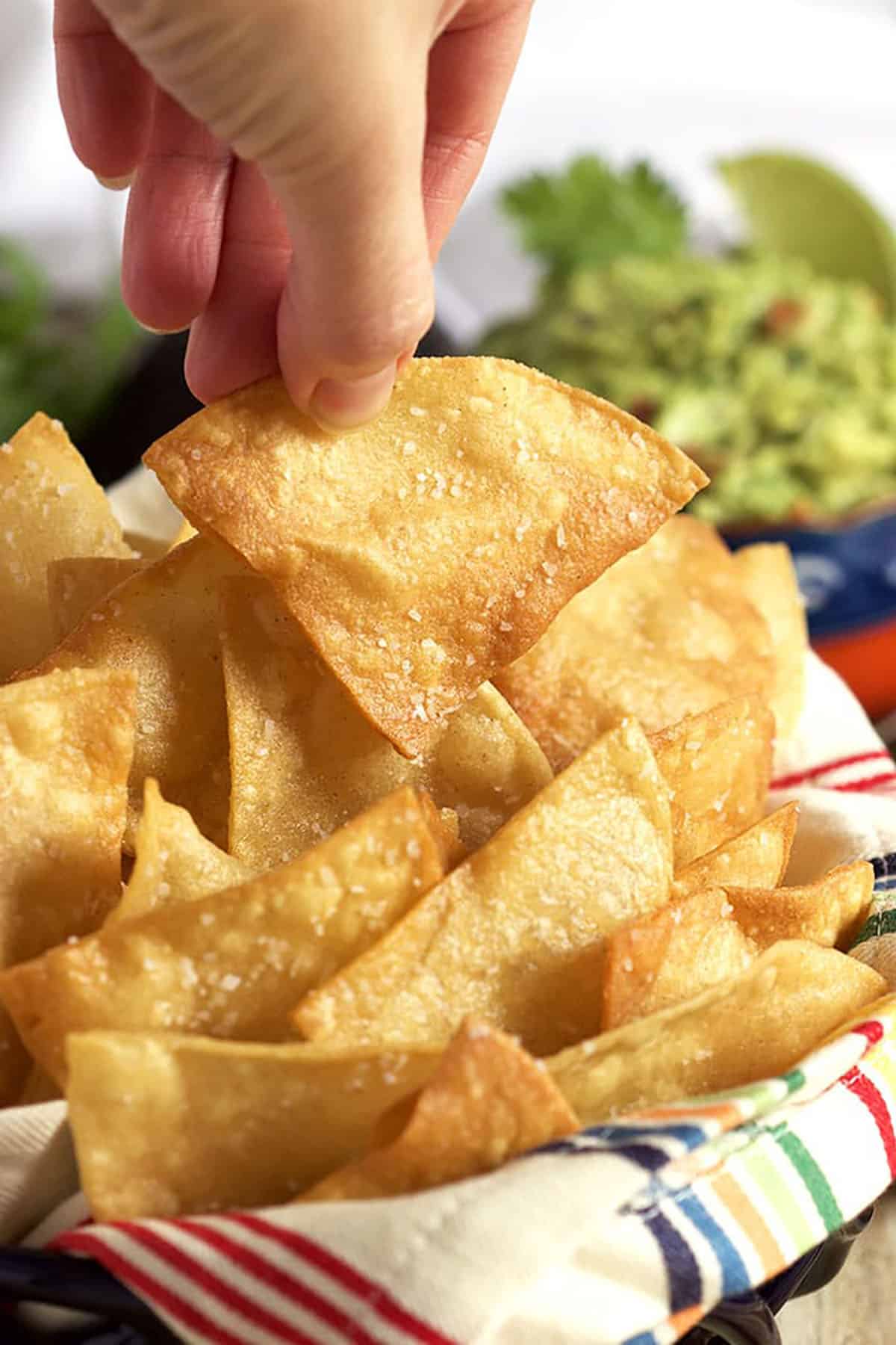 A hand picking up a tortilla chip from a bowl of tortilla chips.