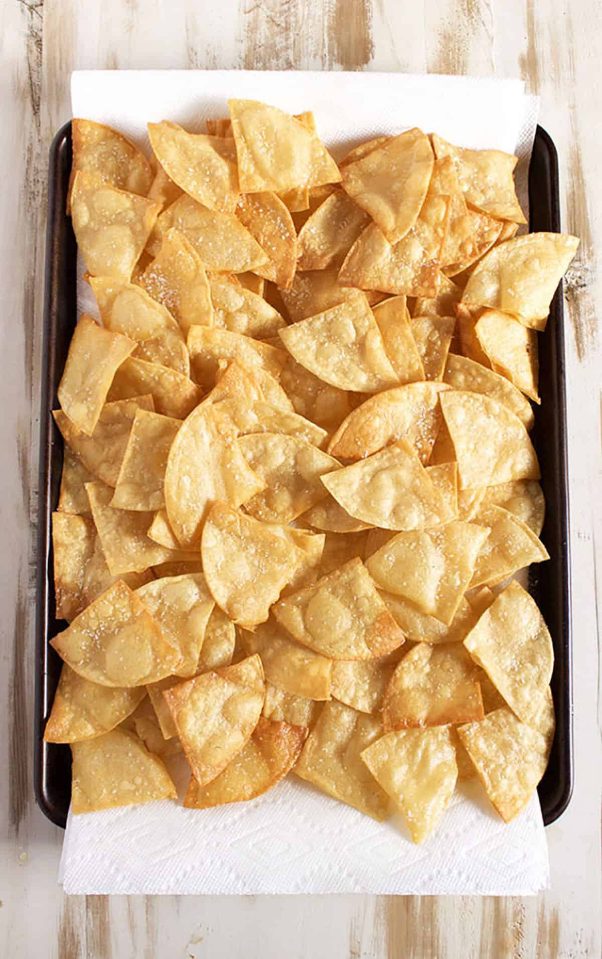 Tortilla chips on a baking sheet with a paper towel under them.