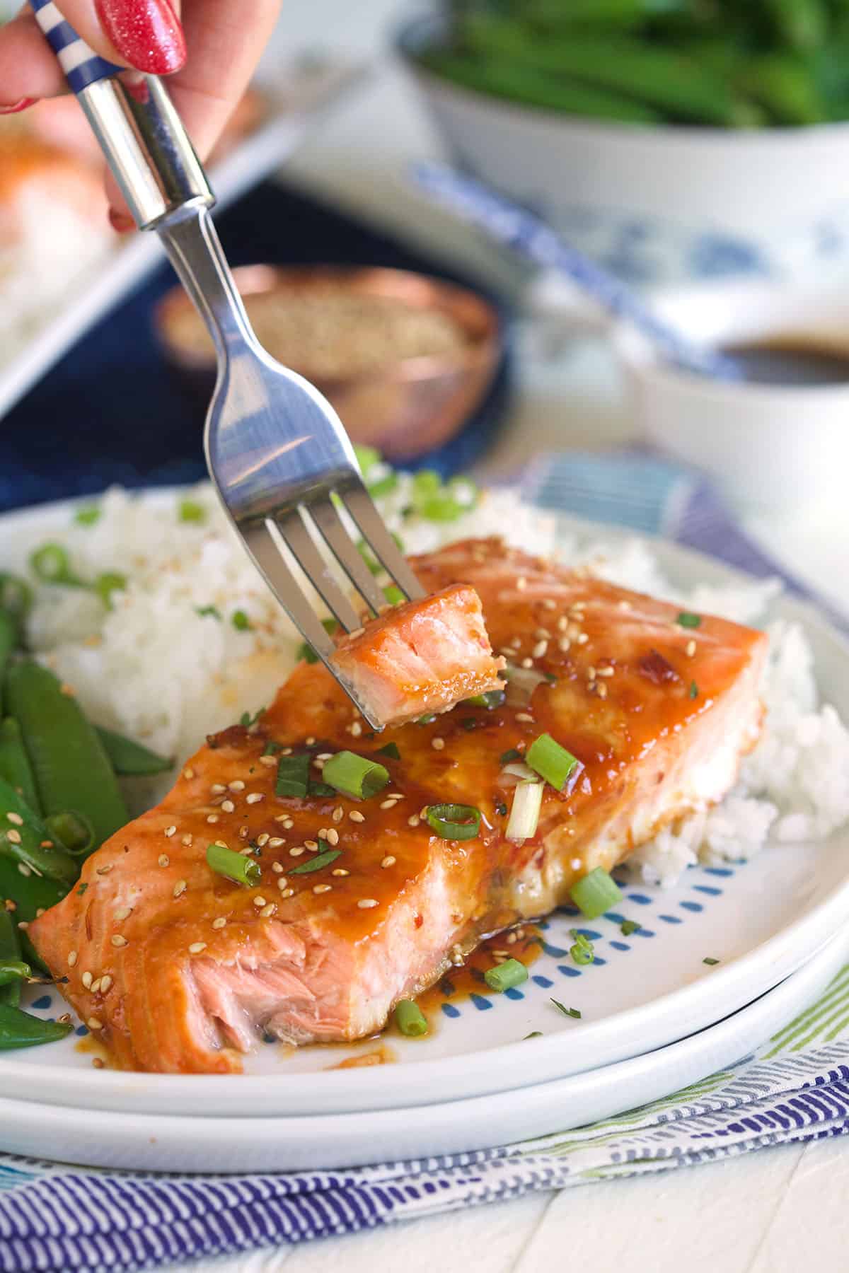 A bite sized portion of salmon is being lifted from the plate by a fork.