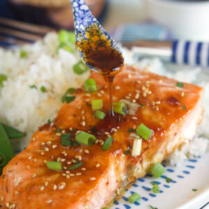 A cooked salmon filet next to a serving of rice is being topped off with more glaze.