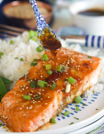 A cooked salmon filet next to a serving of rice is being topped off with more glaze.