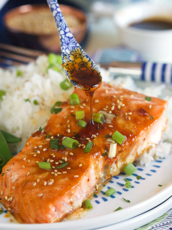 A cooked salmon filet next to a serving of rice is being topped off with more glaze.