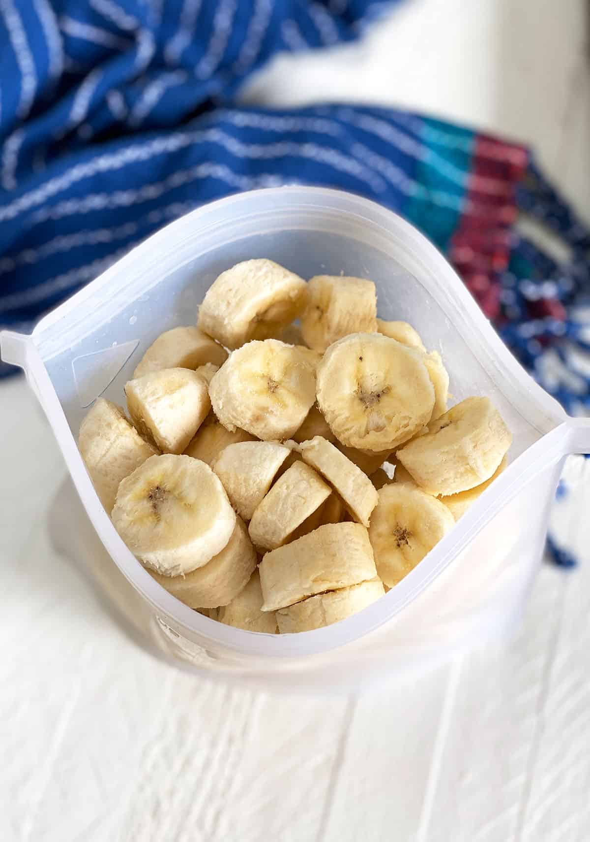 A reusable ziptop bag is open, showing a serving of sliced frozen bananas.