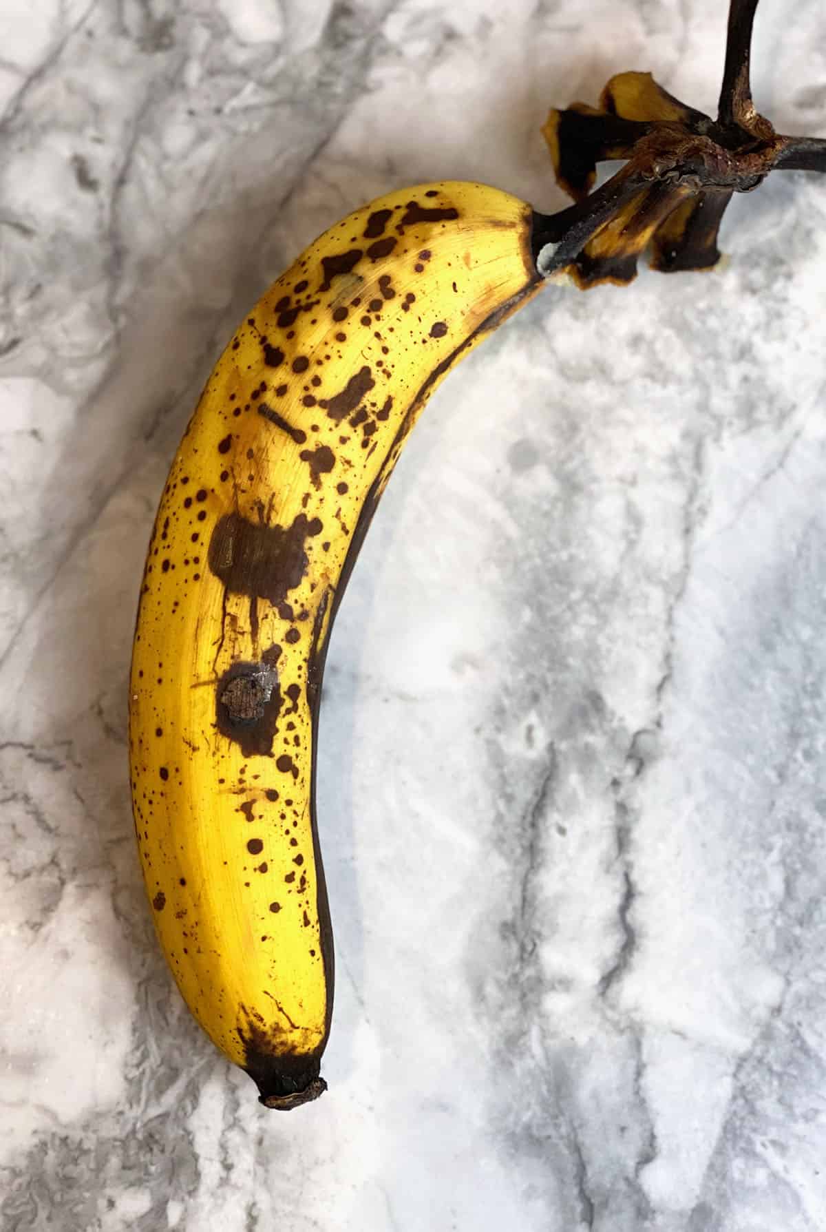 A very ripe banana is presented on a marble surface.