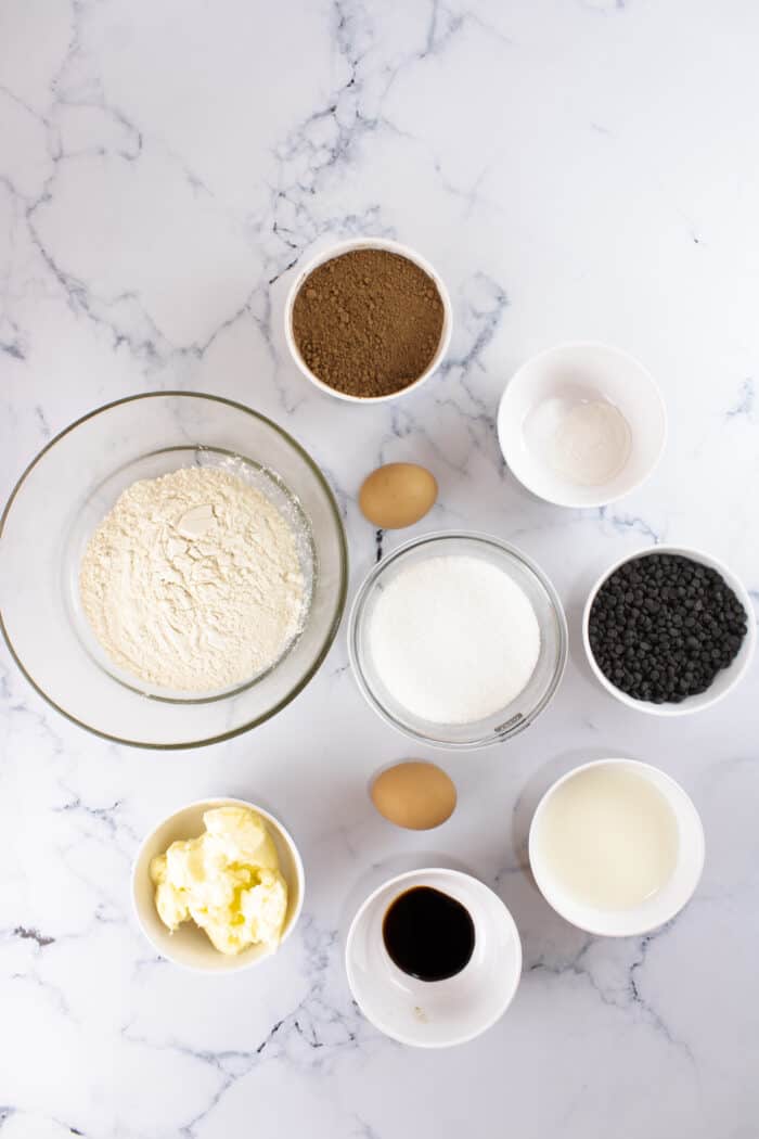 The ingredients for chocolate muffins are presented on a white marble surface.