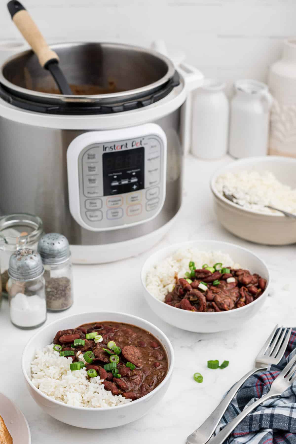 The instant pot is placed behind two full bowls of cooked red beans and rice.