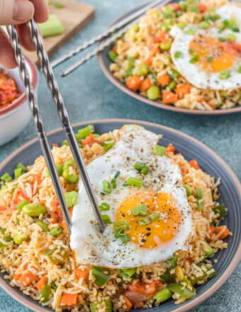 Kimchi fried rice is served with a fried egg and is being eaten with chopsticks from a large plate.