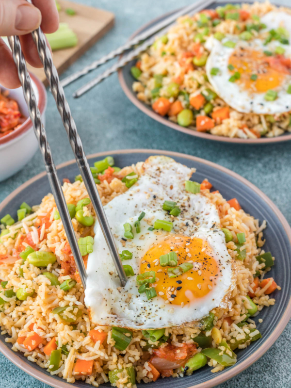 Kimchi fried rice is served with a fried egg and is being eaten with chopsticks from a large plate.