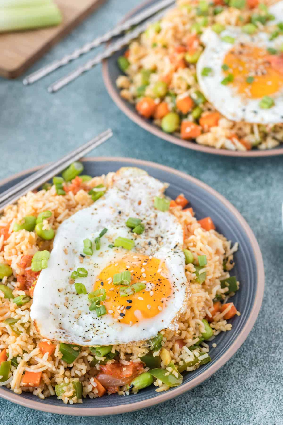 Two bowls of kimchi fried rice are topped with fried eggs.