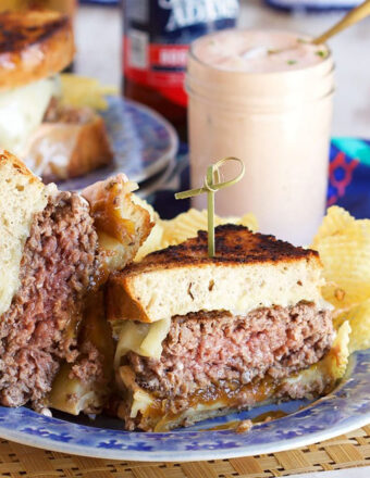 Patty Melt Sandwich cut in half and arranged on a blue plate with a jar of dressing in the background.