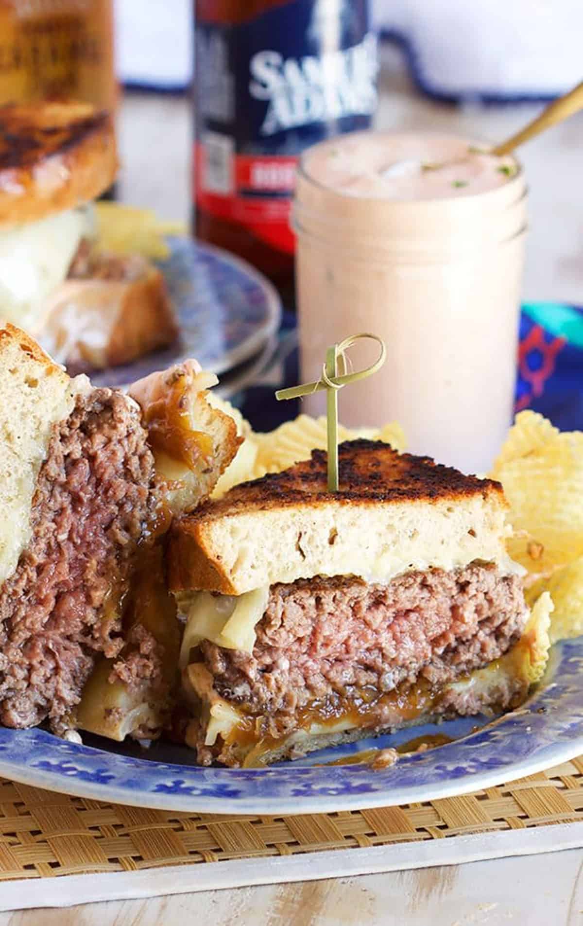 Patty Melt Sandwich cut in half and arranged on a blue plate with a jar of dressing in the background.