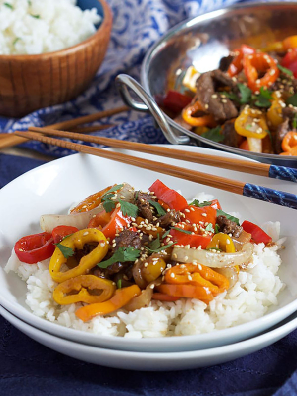 Pepper Steak on white rice in a white shallow bowl with chopsticks resting on top.