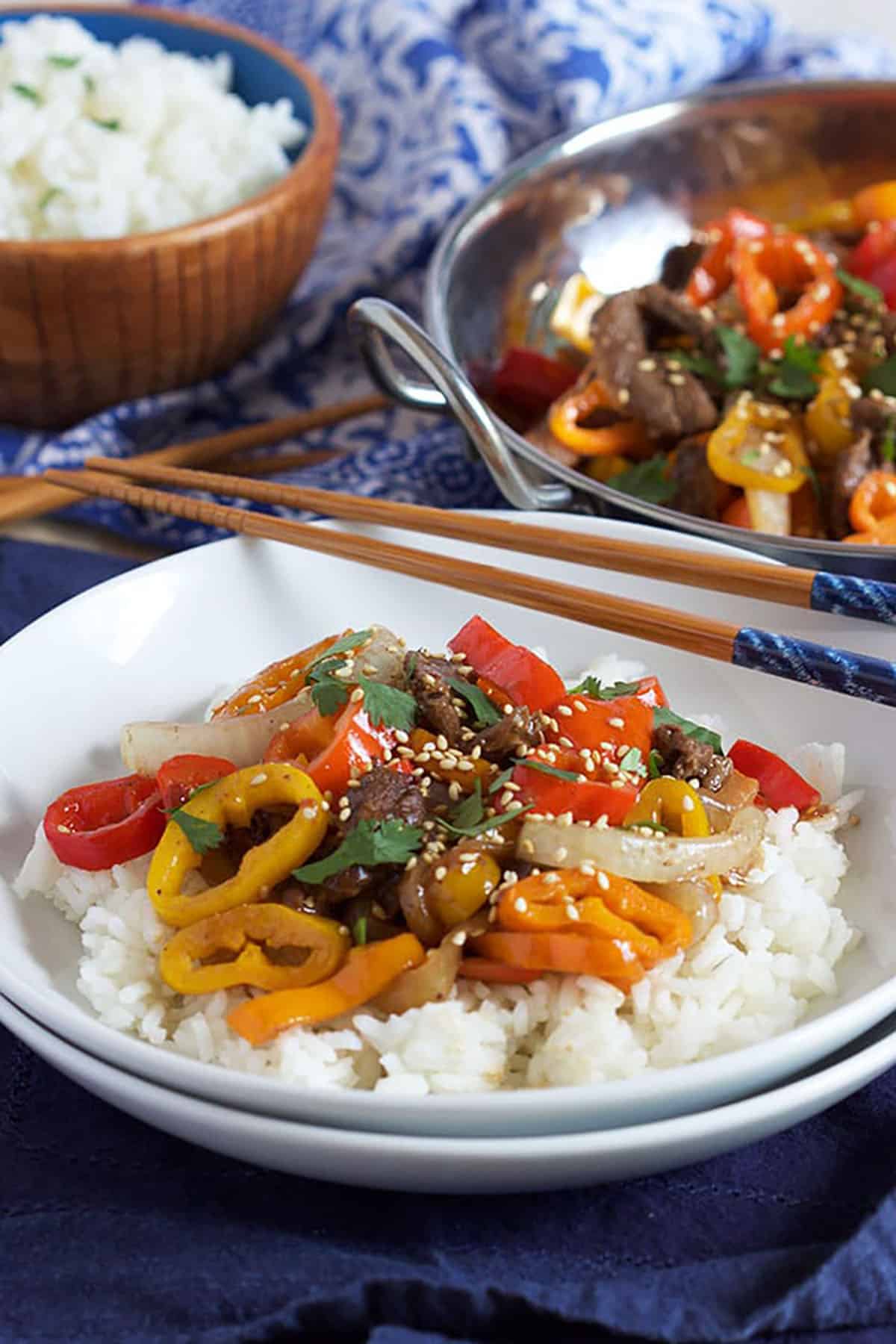 Pepper Steak on white rice in a white shallow bowl with chopsticks resting on top.