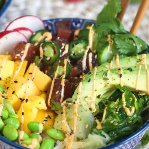 A close up image of a poke bowl shows the tuna and veggies covered in sesame seeds and spicy mayo.